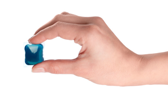 The image shows a hand holding a blue laundry detergent pod. Laundry detergent pods are small, pre-measured packets of detergent encased in a dissolvable film, designed for convenient use in washing machines.