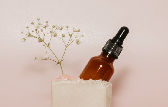 Brown glass dropper bottle with skincare essence oil and small white flowers on a pink background.