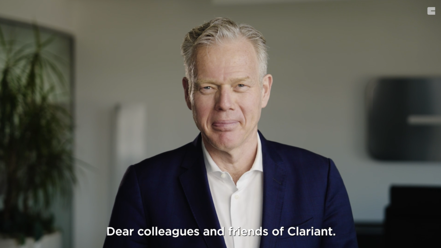 The image shows a person wearing a dark suit and a white shirt, standing in a professional setting. The text at the bottom reads, "Dear colleagues and friends of Clariant." This suggests that the person is addressing an audience associated with Clariant, likely in a formal or corporate communication.