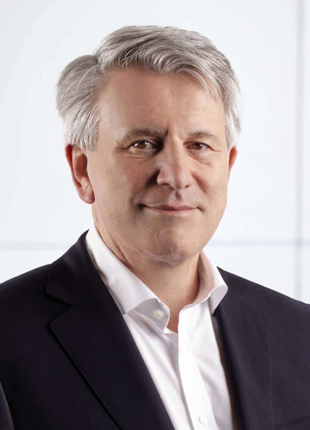 Portrait of a middle-aged man with gray hair wearing a white shirt and dark blazer against a light background.