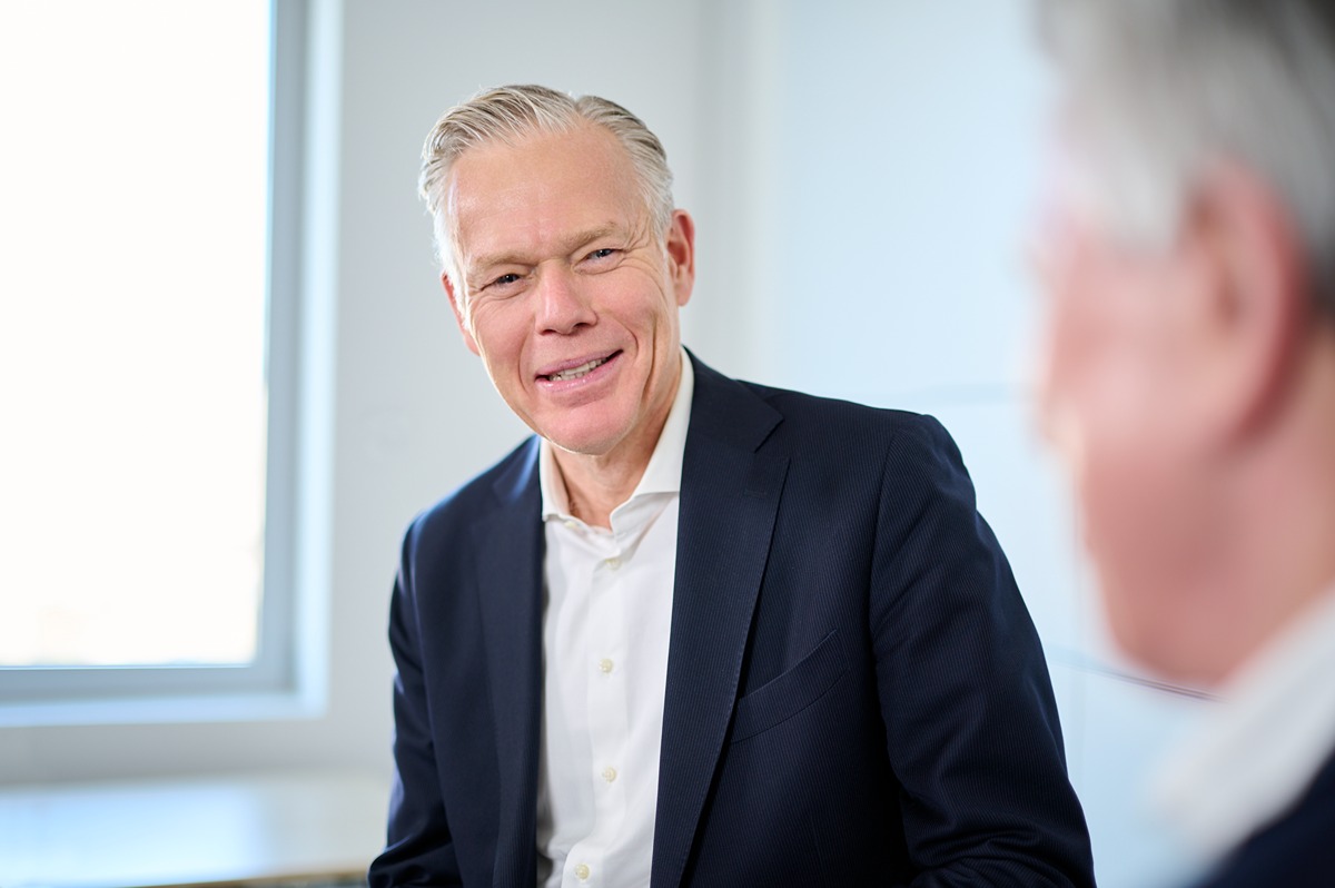 Two men in business attire engaged in a conversation in a bright office setting.