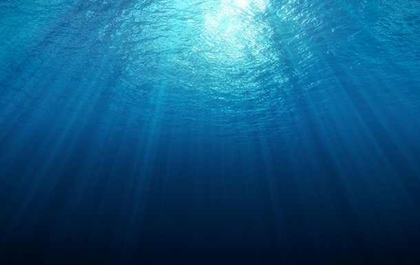 This image shows an underwater scene with sunlight penetrating the water from above. The light rays create a beautiful pattern as they filter through the water, illuminating the upper part of the ocean while the lower part fades into darkness. The water appears clear and blue, giving a sense of depth and tranquility.